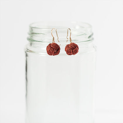 Pair of textured red spherical earrings with gold hooks displayed on a clear glass jar
