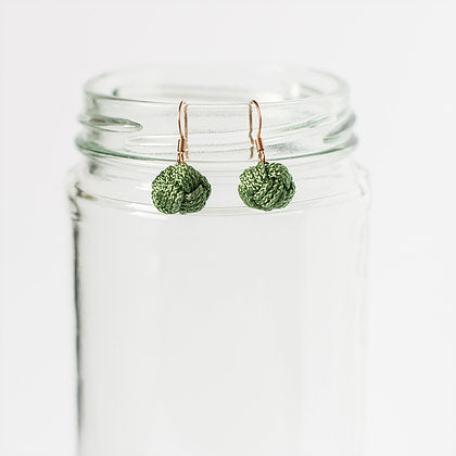 Green textured ball earrings with gold hooks displayed on a clear glass jar, minimalist style